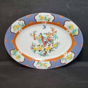 May include: Oval serving platter with a white center featuring a colorful bird and floral design. The border has a blue scale pattern, orange trim, and floral accents. A decorative piece for serving food.
