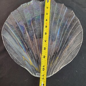 May include: A clear glass serving dish shaped like a seashell with iridescent detailing. The dish is approximately 10 inches wide.