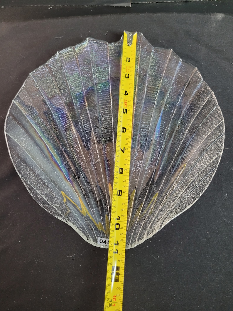 May include: A clear glass serving dish shaped like a seashell with iridescent detailing. The dish is approximately 10 inches wide.