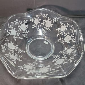 Puede incluir: Cuenco de vidrio transparente con borde festoneado y un patrón floral de rosas grabado alrededor del borde. El cuenco tiene una base circular y es adecuado para servir ensaladas, frutas u otros platos.