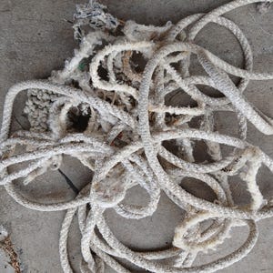 May include: A pile of white rope with frayed ends, tangled and knotted together. The rope is made of a thick, woven material and appears to be old and worn.