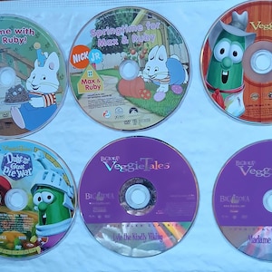 May include: Six DVDs featuring children's shows, including Veggie Tales and Max & Ruby. The DVDs are arranged in two rows of three. The Veggie Tales DVDs are purple with the title in white. The Max & Ruby DVDs are colorful with the titles in white.