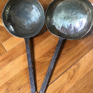 May include: Two antique copper ladles with long, hammered iron handles. The ladles have a worn, aged patina and are perfect for rustic kitchen decor.