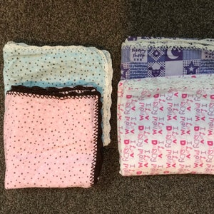 May include: Two baby blankets with crocheted edges. One blanket is pink with brown polka dots and the other is white with pink text that says "I love my mommy and daddy".