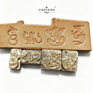 May include: Four rectangular metal stamps featuring dragon designs, positioned below a strip of tan leather embossed with the same four dragon patterns. The text "The FIRSTNINA Design" is printed in black above the leather strip on a white background.