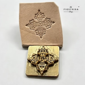 May include: A square brass metal stamp featuring an intricate embossed vajra design, positioned below a piece of light tan leather showing the same stamped pattern. The text "The FIRSTNINA Design" is printed in the upper right corner of the image.