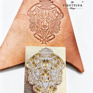 May include: A rectangular brass metal stamp featuring an intricate wolf head design with a Harley-Davidson logo above it. The stamp is positioned below a piece of tan leather that shows the same wolf and logo design embossed into the surface.