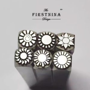 May include: A set of six silver-toned metal stamping tools arranged in a cluster. Each tool features a unique sun-inspired design on its face, including spiral, petal, and ray patterns. The text "The FIRSTNINA Design" is printed above the tools.