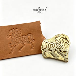 Peut inclure: Un tampon en laiton représentant un cheval stylisé avec des motifs en spirale, placé à côté d'un morceau de cuir beige montrant le même motif de cheval gaufré sur la surface. Le texte "The FIRSTNINA Design" est imprimé au-dessus des objets.