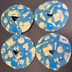 Pu&ograve; includere: Quattro cerchi di tessuto blu e bianco con un bottone bianco al centro. Il tessuto ha un motivo di palline da baseball bianche, mazze, maglie e stelle su uno sfondo blu.