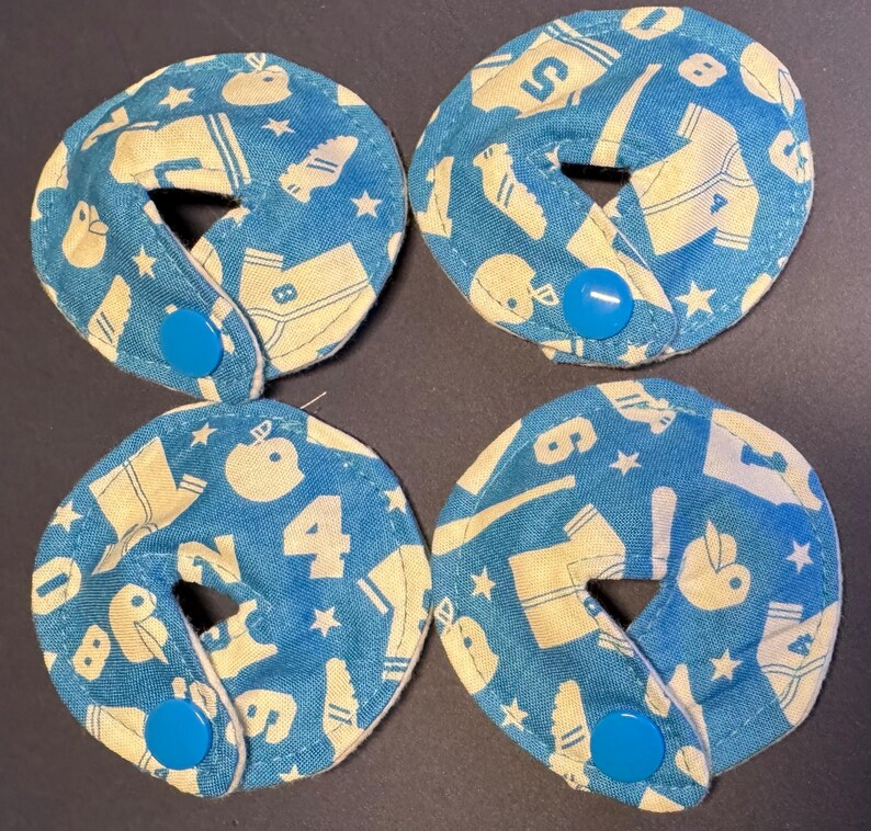 Pu&ograve; includere: Quattro cerchi di tessuto blu e bianco con un bottone bianco al centro. Il tessuto ha un motivo di palline da baseball bianche, mazze, maglie e stelle su uno sfondo blu.