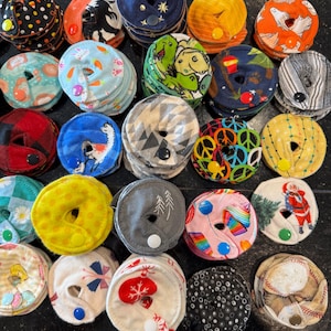 May include: A collection of colorful fabric circles with various patterns and designs. Each circle has a button in the center and is stacked on top of each other. The circles are arranged in a semi-circle on a black surface.