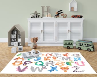 May include: A white rug with the alphabet, each letter designed as a different animal. The rug is on a wooden floor, with a white cabinet and various toy cars and blocks in the background. The letters are in various colors.