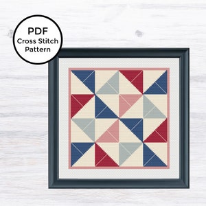 May include: A cross stitch pattern featuring a geometric design with red, blue, and pink triangles on a cream background. The pattern is framed in a black frame.