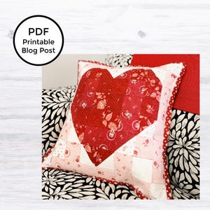 May include: A red and pink heart-shaped pillow with a patchwork design. The pillow is on a black and white patterned couch.