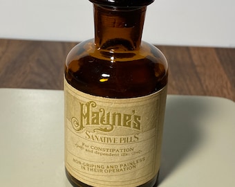 May include: A small, amber glass bottle with a cork stopper. The bottle has a label that reads "Mayne's Sanative Pills For Constipation and dependent ills: Non-Gripping and Painless in their Operation."