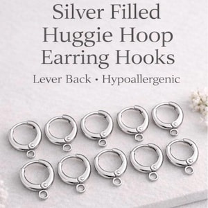 May include: A collection of silver-filled huggie hoop earring hooks. The image shows multiple silver-colored, round earrings with a lever back closure and a small loop at the bottom. The text in the image reads "Silver Filled Huggie Hoop Earring Hooks."