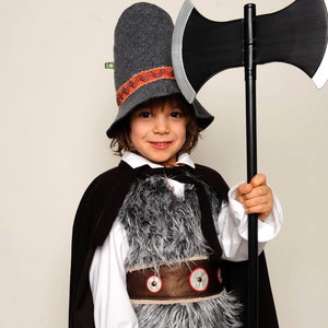 May include: A costume featuring a dark gray felt hat with an orange zigzag band, a black cape, a white long-sleeved shirt, a gray faux fur vest with a brown belt featuring silver studs, brown pants, and a large black double-headed toy battle axe.