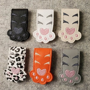 May include: Ten colorful embroidered cat paw bookmarks with different patterns. The bookmarks are made of felt and have a pink heart on each paw.