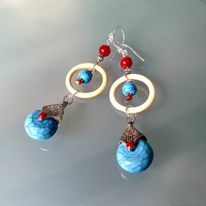 Può includere: Un paio di orecchini pendenti con perline turchesi e rosse. Gli orecchini presentano un anello d'argento con una perla bianca e una goccia turchese.