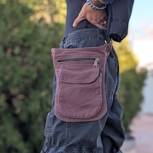 May include: A burgundy hip bag with a zippered main compartment and a front pocket. The bag is worn around the waist and is made of a durable fabric. The person is wearing dark pants.