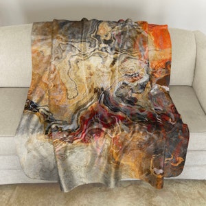 May include: A soft, plush throw blanket with a colorful abstract pattern featuring swirling lines and shades of brown, orange, red, and gray. The blanket is folded and draped over a couch.