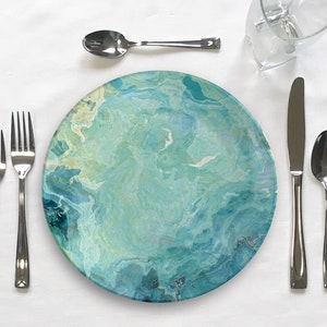 Op de afbeelding: Een blauw en groen swirl-patroon dinerbord met een zilveren vork, mes en lepel op een wit tafelkleed.