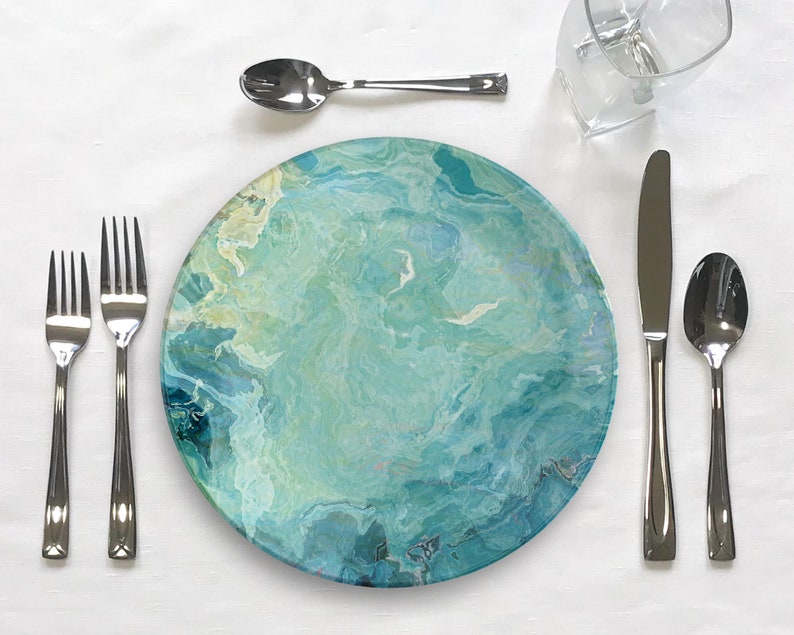 Op de afbeelding: Een blauw en groen swirl-patroon dinerbord met een zilveren vork, mes en lepel op een wit tafelkleed.