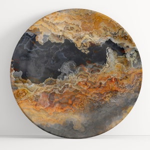 May include: A round decorative plate with a swirling pattern of black, brown, orange, and white. The plate has a smooth, glossy finish.