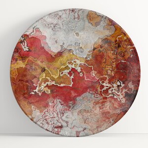 May include: A round decorative plate with a marbled design. The plate features a blend of red, gold, and silver tones, creating a unique, abstract pattern. The plate's surface has a glossy finish, enhancing the colors and design.