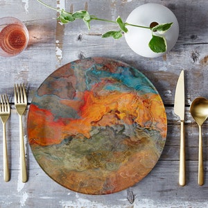 Puede incluir: Un plato redondo y colorido con un dise&ntilde;o de m&aacute;rmol en tonos naranja, marr&oacute;n, azul y verde. El plato est&aacute; colocado sobre una mesa de madera con cubiertos de oro y una copa de vino.