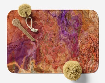 Può includere: Un tappetino da bagno con un design astratto che presenta motivi a spirale in tonalità di arancione, rosso, viola e marrone. Il tappetino è decorato con due accessori da bagno, una spazzola di legno e una spugna.