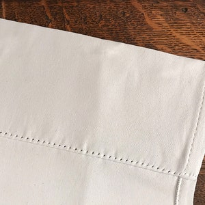 Pu&ograve; includere: Primo piano di un tessuto bianco con un bordo cucito. Il tessuto ha una texture sottile ed &egrave; leggermente stropicciato.