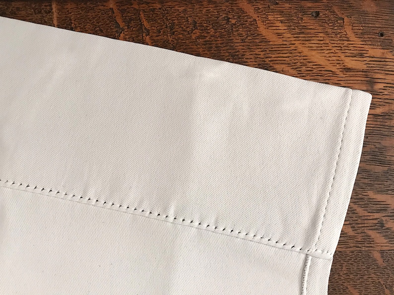 Pu&ograve; includere: Primo piano di un tessuto bianco con un bordo cucito. Il tessuto ha una texture sottile ed &egrave; leggermente stropicciato.