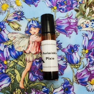 May include: A small brown glass bottle with a black roll-on top. The bottle is labeled "Periwinkle Pixie" and has a floral design on the background.