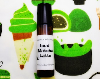May include: A small brown glass bottle with a black roll-on top. The bottle has a white label with the text "Iced Matcha Latte" and the website address "thesoawhiteowl.etsy.com".
