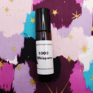 May include: A small, clear glass bottle with a black cap and a white label. The label reads "1000 Whispers" and includes the website "snowywhiteowl.etsy.com".