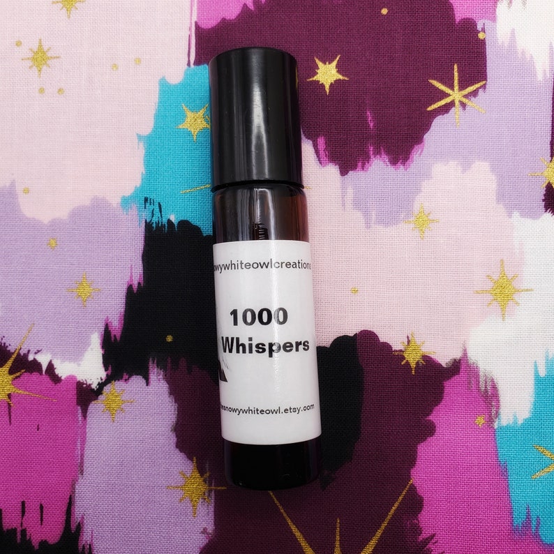 May include: A small, clear glass bottle with a black cap and a white label. The label reads "1000 Whispers" and includes the website "snowywhiteowl.etsy.com".