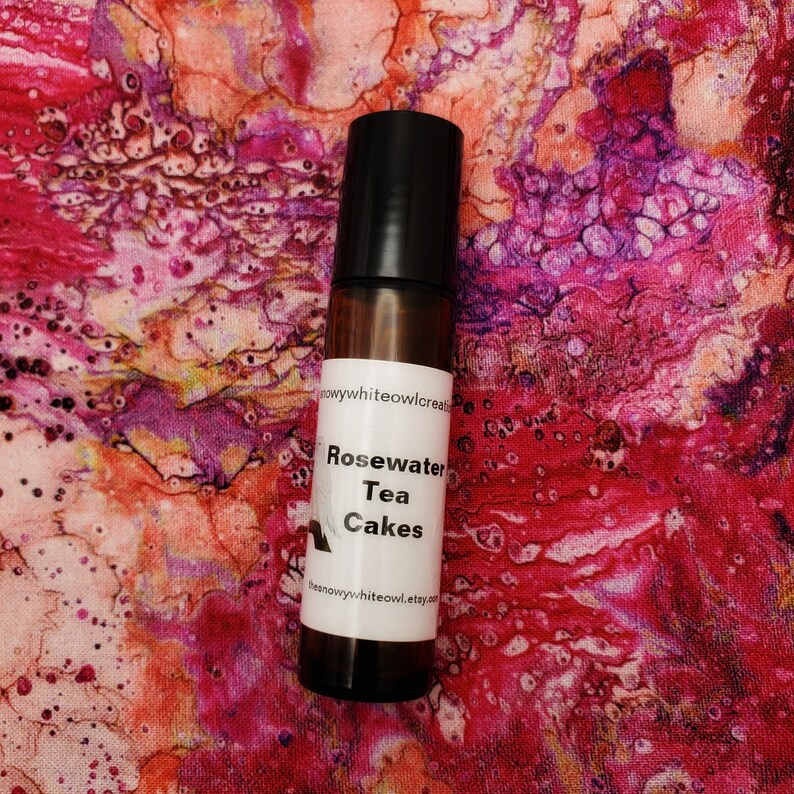 May include: A brown glass roller bottle with a black cap and a white label that reads "Rosewater Tea Cakes" and "thesnowywhiteowl.etsy.com".