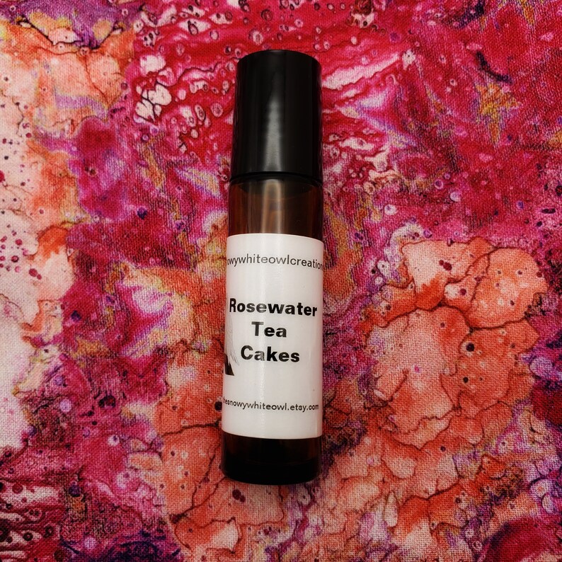 May include: A brown glass bottle with a black cap and a white label. The label says "Rosewater Tea Cakes" and "snowywhiteowl.etsy.com".