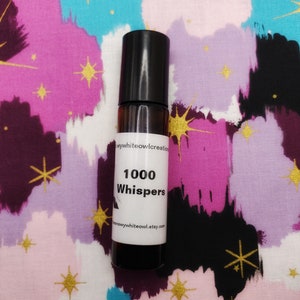 May include: A small brown glass bottle with a black rollerball top. The bottle has a white label with the text "1000 Whispers" and the website address "snowywhiteowl.etsy.com".