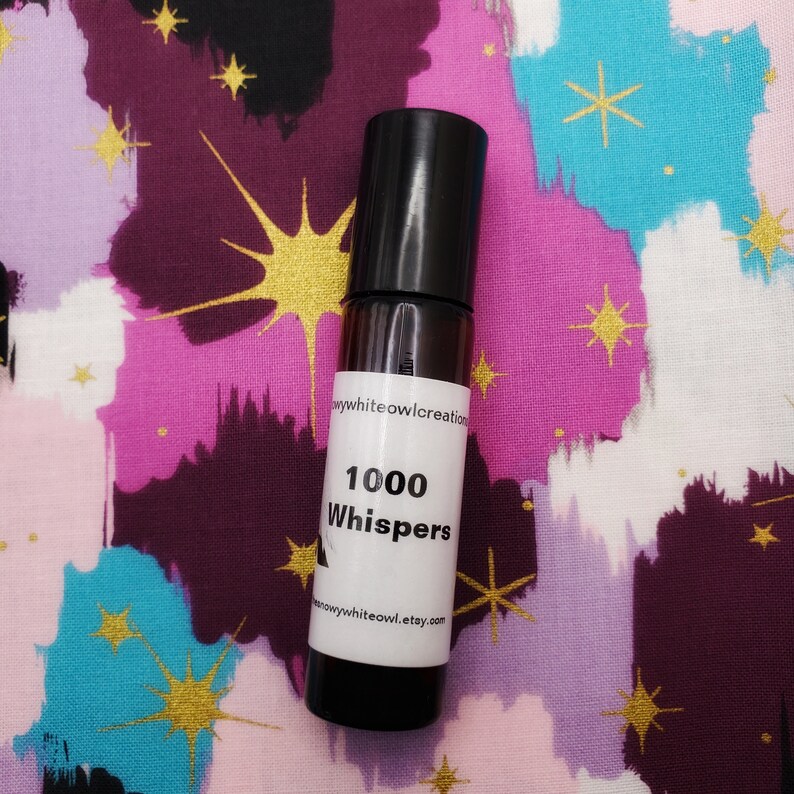 May include: A small, clear glass bottle with a black cap and a white label. The label reads "1000 Whispers" and "snowywhiteowl.etsy.com".