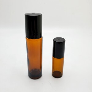 May include: Two amber glass roller bottles with black lids. The larger bottle is about twice the size of the smaller bottle.
