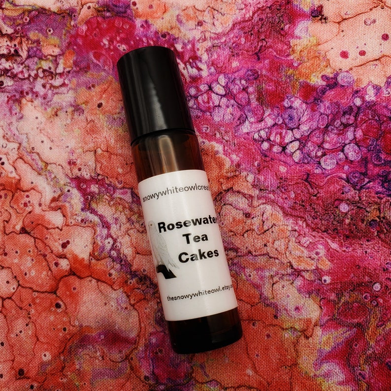 May include: A brown glass roller bottle with a black cap and a white label that says "Rosewater Tea Cakes" and "thesnowywhiteowl.etsy.com".