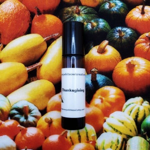 May include: A black roller bottle with a white label that reads "Thanksgiving" against a backdrop of colorful gourds. The bottle has a black cap and a clear glass body, and the background features various pumpkins.