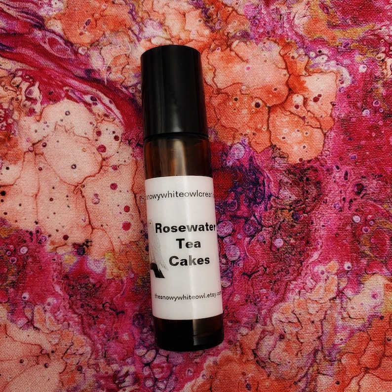 May include: A brown glass roller bottle with a black cap. The label reads "Rosewater Tea Cakes" and "thesnowywhiteowl.etsy.com".