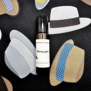 May include: A brown glass bottle of perfume with a black cap and a white label. The label says "teowlperfumery" and "Swagger".