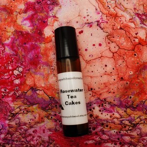 May include: A small brown glass bottle with a black cap and a white label. The label says "Rosewater Tea Cakes" and includes the website "etsy.com".