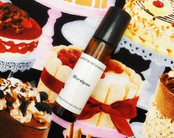 May include: A small brown glass bottle with a black cap and a white label that says "Marzipan". The bottle is on a black background with a pattern of colorful cakes and pastries.