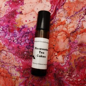May include: A brown glass roller bottle with a black cap and a white label that reads "Rosewater Tea Cakes" and "thesnowywhiteowl.etsy.com".